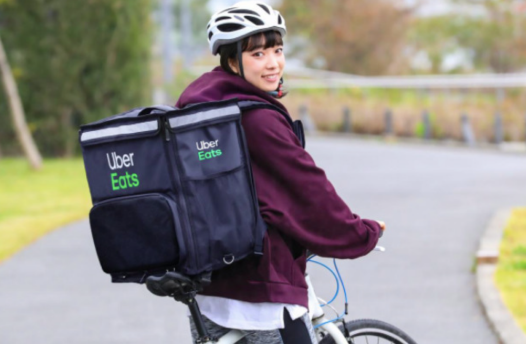 Uber Eats のバッグを背負って自転車で配達する女性